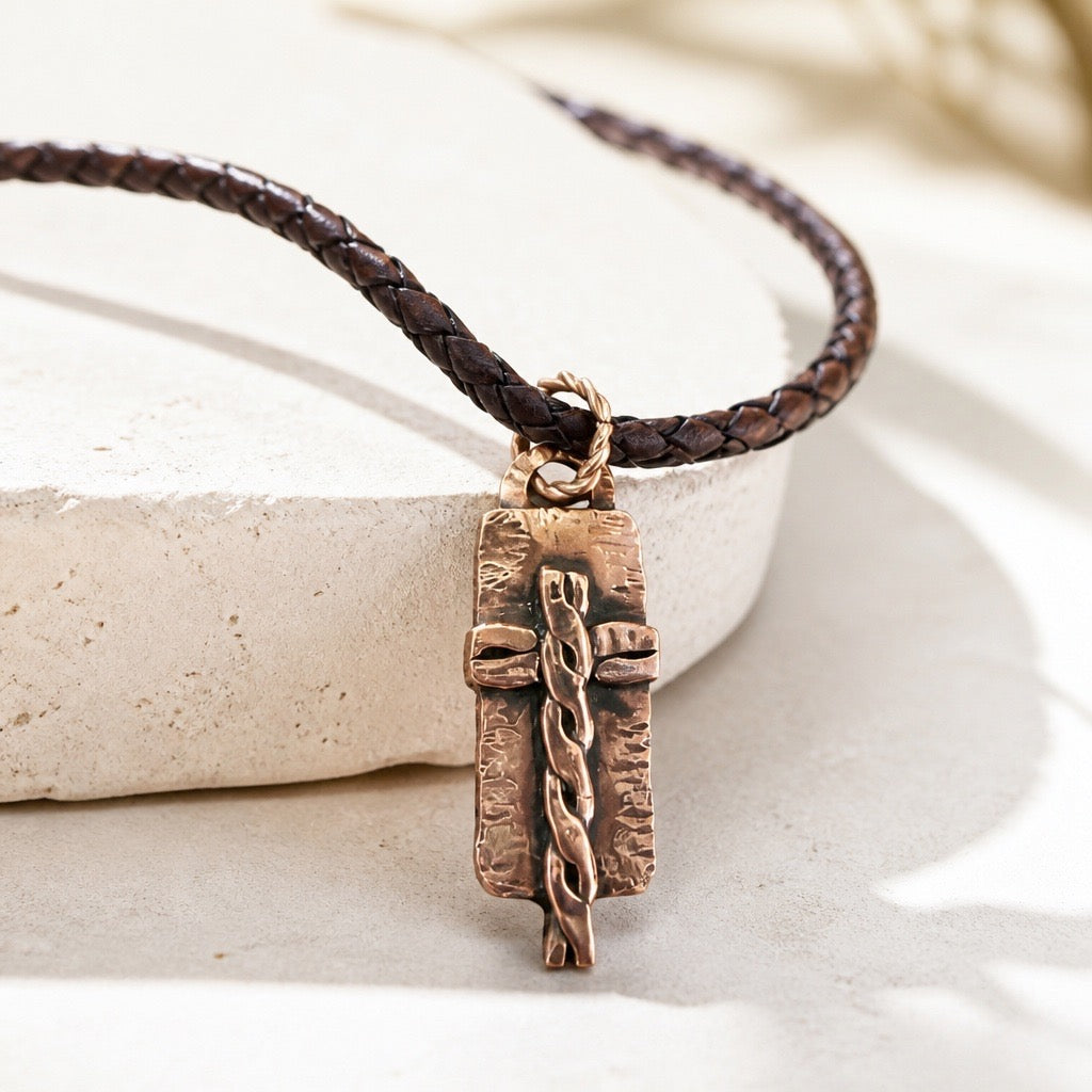 Hand-forged copper cross necklace by Ginny Taylor Designs, showing layered copper detail and antiqued finish on dark braided leather cord. 
